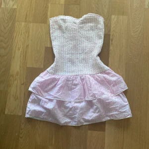 Rosa volangklänning från Gina Tricot - Supersöt rosa kortklänning från Gina Tricot med smockad överdel och dubbla volanger i kjolen. Axelbandslös modell med ljusa toner och diskret mönster. Perfekt för dig som vill ha en feminin och lekfull stil! 💕