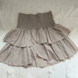 Beige volangkjol från Neo Noir - Supersöt beige kortkjol från Neo Noir med bred smock i midjan och flera lager volanger. Xs/s