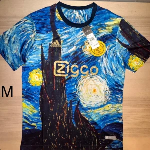 Ajax x Van Gogh  - Stick ut i sommarvärmen med denna exklusiva Ajax-tröja designad i samarbete med Van Gogh-museet! Denna limiterade upplaga från Adidas kombinerar fotbollskultur med ikonisk konst – ett måste för både samlare och stilmedvetna fans. Tröjan har en tryck inspirerad av Van Goghs mästerverk Stjärnenatt, komplett med Ajax-emblem och Ziggo-sponsormärke i guld. Perfekt för matchdag, streetwear eller som unik present.