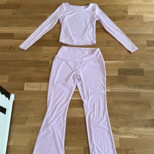 Ljusrosa set med långärmad topp och byxor - Säljer ett ljusrosa set med en långärmad topp och matchande byxor. Toppen är croppad och byxorna har en hög midja. Perfekt för en avslappnad dag eller träning. Materialet är mjukt och stretchigt för extra komfort.