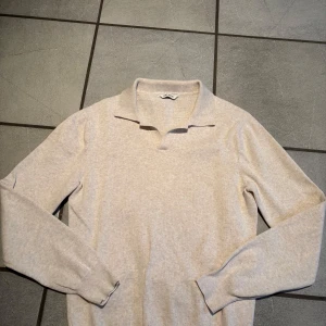 Beige tröja från John Henric - Säljer en stilren beige tröja från John Henric. Tröjan har en klassisk krage och långa ärmar, perfekt för en elegant look. Den är tillverkad i 100% bomull som ger en bekväm passform.