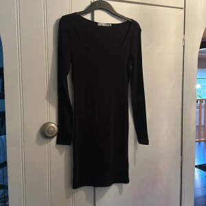 Svart klänning från 157 - Snygg svart klänning från 157 med långärmad design. Perfekt för en stilren look. Klänningen har en tight passform och är tillverkad i ett ribbat material.