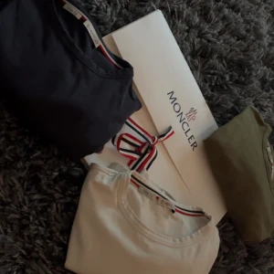 T-shirt från Moncler - Säljer en stilren t-shirt från Moncler i flera färger: svart, olivgrön och vit. T-shirten har korta ärmar och en liten Moncler-logga på ärmen. Perfekt för en casual look med en touch av lyx. Köp en för 650, två för 1200 eller tre för 1850 kr