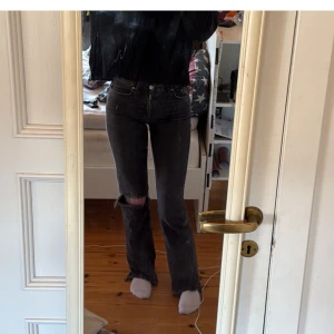 Svarta bootcut jeans med hål  - Snygga svarta jeans med ett hål på ena knät. Medelhög midja. Tror ej de finns o köpa längre. Storlek 34. Lite slitning nere vid fötterna som ska vara så, inget jag gjort själv. Skriv för frågor!