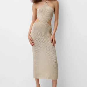 Beige stickad klänning med öppen rygg - Helt oanvänd! Beige, något glittrig, klänning med stickat mönster och öppen rygg. Den har knytning i ryggen samt i nacken. Ganska liten i storleken och saknar stretch, i strl S.