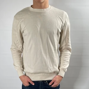 Beige tröja från Oscar Jacobson - Säljer en stilren beige tröja från Oscar Jacobson i meriono ull, tillverkad i Italien. Tröjan har en klassisk rund hals och långa ärmar med ribbade muddar. Perfekt för en elegant och avslappnad look.