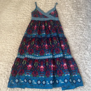 Blommig klänning från H&M - STOR I STOLEK!! Charmig blommig klänning från H&M med smala axelband och omlott-design. Klänningen har ett färgglatt mönster i blått, rosa och grönt med vita detaljer. Perfekt för sommarens varma dagar.