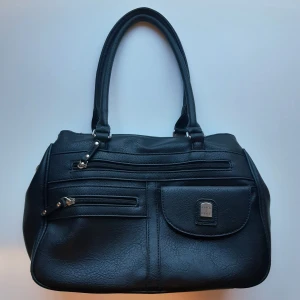 Svart handväska - Snygg svart handväska som har flera praktiska fack med dragkedjor och dubbla handtag. Den har tre stora fack, där ett av dem har ytterligare två fickor och ett har ett innerfack, samt fyra ytterfack - otroligt praktisk väska! Har används en gång. Pris går alltid att diskutera. Hör av dig om du undrar något! 😊