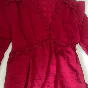 Röd blus från Na-kd - Snygg röd blus från Na-kd med volangdetaljer och v-ringning. Förgen är lite mer åt det vinröda hållet i verkligheten har långa ärmar och en smickrande passform. Perfekt för att sticka ut med stil!