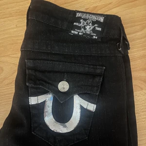 Svarta jeans från True Religion - Snygga svarta jeans från True med cool glitter design på fickorna. Storlek 27. Avklippta där nere. 