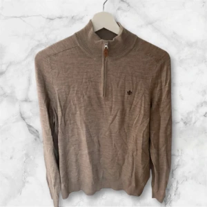 Beige merinoulltröja från Morris - Säljer en stilren beige tröja från Morris i 100% merinoull. Tröjan har en halv dragkedja och en liten broderad logga på bröstet. Perfekt för kyligare dagar med sin mjuka och varma känsla. 🧥