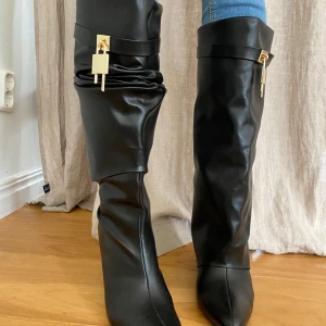 Svarta stövlar med gulddetaljer - Snygga svarta stövlar i skinn med spetsig tå och dekorativa gulddetaljer. Stövlarna har en gömd dragkedja och en unik design med veckad effekt som man kan vika lite som man vill. Skorna har aldrig använts utomhus, de har endast provats inomhus. Det är storlek 39 men känns mer som en 38,5. Klacken är 7 cm hög. 