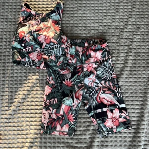 Stronger träningsset - Snygg set med tropiskt blommönster och flamingos. Toppen har korsade band och textdetaljer som 'FIESTA' och 'JAZZ!'. Perfekt för ett gympass💖