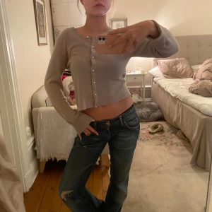 Beige kofta med knappar - Säljer en stilren beige kofta med knappar framtill. Koftan är croppad och har långa ärmar, perfekt för en avslappnad look. Passar bra till jeans eller kjol.