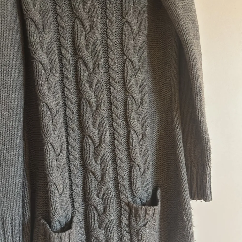 Säljer en mysig grå stickad klänning från Bonprix med kabelstickat mönster och stor krage. Tröjan har långa ärmar och praktiska fickor framtill. Perfekt för kyliga dagar! 🧶. Mekot.