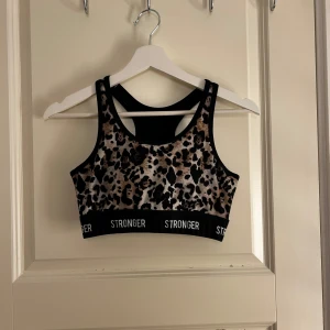 Leopardmönstrad sporttopp från Stronger - Snygg leopardmönstrad sporttopp från Stronger med breda axelband och elastisk kant med logga. Perfekt för träning och ger bra stöd. 🐆