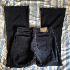 Svarta manchesterbyxor från Wrangler - Snygga svarta manchesterbyxor från Wrangler med bootcut-stil. Byxorna har en klassisk femficksdesign och är perfekta för en stilren look. De är tillverkade i mjukt manchestertyg som ger en skön känsla.