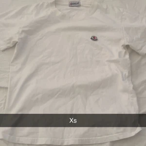Vit t-shirt från Moncler - Säljer en stilren vit t-shirt från Moncler med korta ärmar och en liten logga på bröstet. Perfekt för en avslappnad look. Passar bra till jeans eller shorts. 🕶️