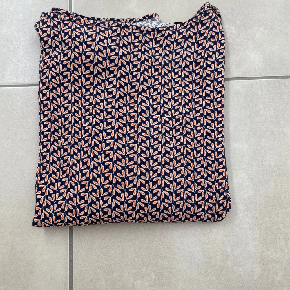 Jättefin mörkblå blus med orangefärgat bladmönster från Esprit. Passar perfekt nu till våren! Den har en boatneck krage och en fin knappdetalj på trekvartsärmarna. 100% viskos.. Puserot.