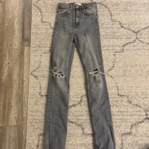 Grå jeans från Zara - Gråa jeans från Zara. Hög midja i storlek 34. Dom är öppnade längst ner och är mer raka än tajta. Sitter bra på mig som är 167cm lång men midjan är för hög på mig som har längre ben än överkropp. 
