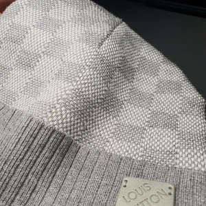 Authentic Louis Vuitton beanie/mössa - Snygg grå mössa från Louis Vuitton med ett diskret rutmönster. Mössan har en ribbad kant och en elegant logotypplatta framtill. Perfekt för att hålla stilen under kyliga dagar. 