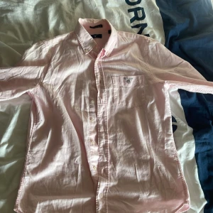 Rosa skjorta från GANT - Säljer en stilren rosa skjorta från GANT med broderad logga på bröstfickan. Skjortan har långa ärmar och knappar framtill. Perfekt för en klassisk och avslappnad look.