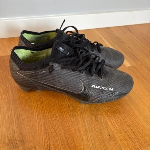 Svarta fotbollsskor från Nike - Snygga svarta Nike fotbollsskor med Zoom-teknologi. Skorna har snörning och en slitstark sula med bra grepp. Perfekta för fotbollsplanen och designade för att ge optimal prestanda.