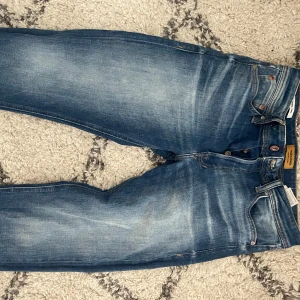 Jack and Jones jeans - Snygga blå jeansbyxor med klassisk femficksdesign och knappgylf och snygga fades. Modellen heter tapered/mike.  De har en lätt tvättad look perfekt  för en avslappnad stil.  Strl: 29:30.