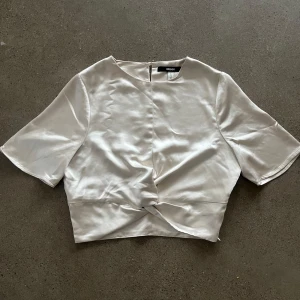 Vit topp från Bik Bok - Säljer en fin vit topp från Bik Bok designad av Lovisa Barkman. Den har korta ärmar och en knytdetalj framtill. Perfekt för middagar och mysiga utekvällar!