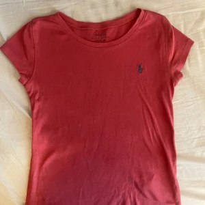 Rosa t-shirt från Ralph Lauren - Säljer en snygg röd t-shirt från Ralph Lauren med det klassiska logotypbroderiet på bröstet. T-shirten är kortärmad och tillverkad i mjuk bomull. Str 140 barn