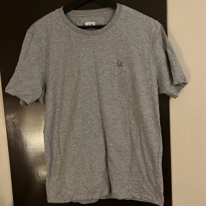 Grå t-shirt från C.P. Company - Säljer en stilren grå t-shirt från C.P. Company. Den har en normal passform och är tillverkad i mjukt bomullsmaterial. Perfekt för en avslappnad look.