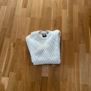 Vit stickad tröja  - Säljer en stilren vit stickad tröja från 1924 med ett klassiskt flätmönster. Tröjan har rund hals och är perfekt för kyligare dagar. Passar både till jeans och kjol för en avslappnad look.