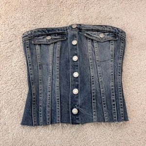 Jeanskorsett från Zara - Säljer en cool jeanskorsett från Zara med knappar framtill och fickdetaljer. Perfekt för att ge en edgy touch till din outfit. 💙