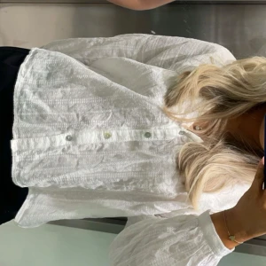Vit blus från Zara - Säljer en stilren vit blus från Zara med diskret prickigt mönster. Blusen har långa ärmar och knappar framtill. Perfekt för en elegant och avslappnad look.