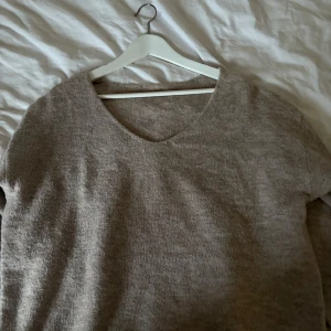 Beige stickad tröja - Säljer en mysig beige stickad tröja med v-ringning. Perfekt för kyliga dagar och enkel att matcha med olika outfits. Tröjan har långa ärmar och en avslappnad passform.