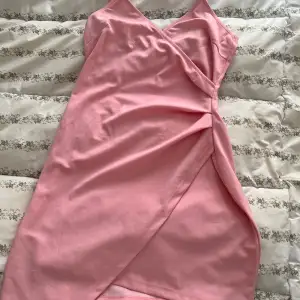 Säljer en söt rosa omlottklänning med smala axelband och v-ringning. Klänningen har en elegant omlottdesign framtill och är perfekt för sommarens varma dagar.              Lite ett litet märke ( bild 2) 