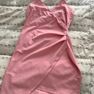 Rosa omlottklänning - Säljer en söt rosa omlottklänning med smala axelband och v-ringning. Klänningen har en elegant omlottdesign framtill och är perfekt för sommarens varma dagar.              Lite ett litet märke ( bild 2) 
