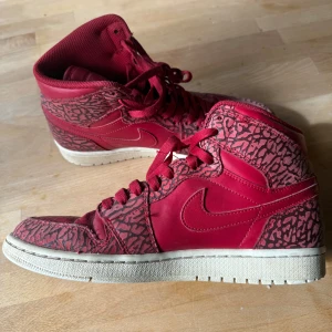  Nike Air Jordans - Snygga röda Nike Air Jordans med ett unikt mönster. Skorna har en klassisk hög design med snörning och en vit sula. Perfekta för dig som vill sticka ut med stil.