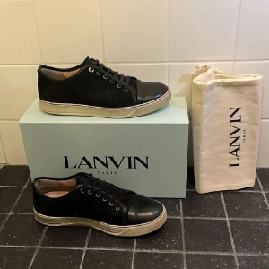 Svarta sneakers från Lanvin - Snygga svarta sneakers från Lanvin med vit sula och snörning. Skorna har en stilren design med en klassisk look. Perfekta för en avslappnad men ändå elegant stil.Storlek UK8~43-44, defekt sula och häl, mvh Sthlms-Arkivet 