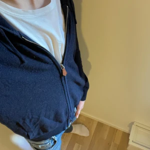 Kashmir hoodie - Säljer en mörkblå hoodie med dragkedja och huva. Tröjan har långa ärmar och ribbade muddar vid ärmslut och nederkant. Perfekt för en avslappnad stil.