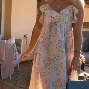 Blommig sommarklänning med volangdetaljer - Säljer en söt och luftig blommig klänning perfekt för sommardagar. Klänningen har volangdetaljer vid axlarna och en lös passform. Den är ärmlös och har en ljus färgton med pastellfärgade blommor.