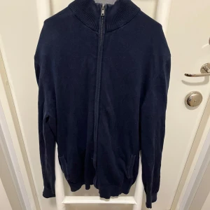 Mörkblå tröja med dragkedja från Pier One - Säljer en stilren mörkblå tröja från Pier One. Tröjan har en dragkedja framtill och en hög krage. Perfekt för kyligare dagar.