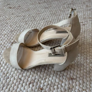 Beigea sandaler med klack och öppen tå - Snygga beige sandaler från Nelly med öppen tå och justerbart spänne runt ankeln. De har en bekväm klack och är perfekta för sommarens alla tillfällen. Är lite smutsiga/slitna samt på sista bilden syns en skada på vänstra klacken!🌷🌷