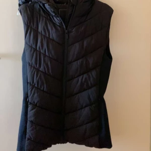  Zara väst - Snygg svart dunväst från Zara med dragkedja och huva. Perfekt för lager-på-lager under kyliga dagar. Västen har en stilren design med quiltade detaljer som ger en modern look.