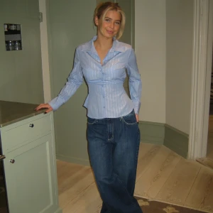 Blå randig skjorta med knyt - Fin blå skjorta med silvriga ränder och knyt i ryggen. Skjortan är från Design By Si och är i nyskick men säljes då den är för liten. Returpolicyn var krånglig därav tittar jag intresse här innan jag annars väljer att returnera. Storleken är M/L, men sitter som en stl S, vilket även står på deras hemsida. 