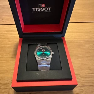 Tissot klocka med grön urtavla - Säljer en elegant Tissot klocka med en iögonfallande grön urtavla. Klockan har ett stilrent silverfärgat armband och kommer i originalförpackning. Perfekt för den som vill ha en tidlös accessoar.