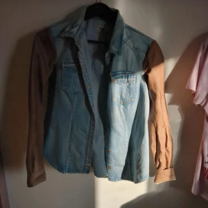 Jeansskjorta med bruna ärmar från ONLY - Säljer en cool jeansskjorta från ONLY med kontrasterande bruna långärmade ärmar. Skjortan har knappar framtill och två bröstfickor. Perfekt för en avslappnad stil med en twist. Passar bra till både jeans och kjol!