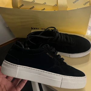  Axel Arigato - Strl 38 - Använda ca 3 gånger. Köpta från Axel Arigato för 2600 kronor. Boxen, dustbag och påsen kommer med. Bilder kan skickas. Då dom är använda ca 3 gånger säljer jag dom för 1800 kr , pris kan diskuteras vid snabb och enkel affär!                                                                  Snygga svarta sneakers från Axel Arigato med en stilren design. Skorna har en vit sula och är tillverkade i mocka. Diskret logotyp i guld på sidan och klassisk snörning framtill.