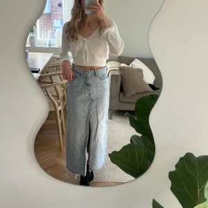Lång jeanskjol från Zara - Snygg lång jeanskjol från Zara i ljusblå denim. Kjolen har en framslits och rå kant nedtill för en trendig look. Perfekt för en avslappnad stil.