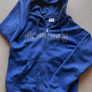 Blå hoodie med dragkedja - Snygg blå hoodie med dragkedja och textdetalj på bröstet. Perfekt för en avslappnad stil. Oklar på märket men det  är perfekt till sommaren, bud och byten är intressant.